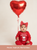 Baby in a red 'My First Valentine's' outfit with a heart-shaped balloon on a beige background.